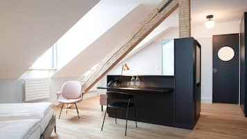 Ett modernt sovrum i loftstil med ett sluttande tak, träbjälkar, ett skrivbord med en lampa och en säng.
