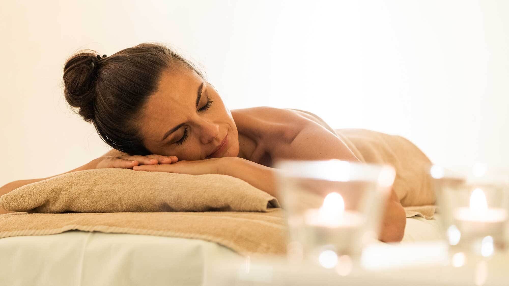 A person lying on a bed with a towel, surrounded by candles.