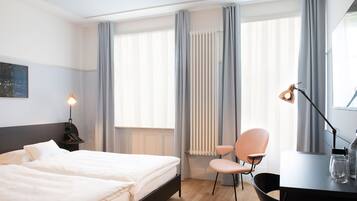 A hotel room with a bed, a desk with a lamp, a chair, and a radiator.