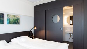 A modern hotel room with a bed, a nightstand with a lamp, a wall-mounted phone, and a bathroom visible through a door. - Hotel Schützen (Rheinfelden)