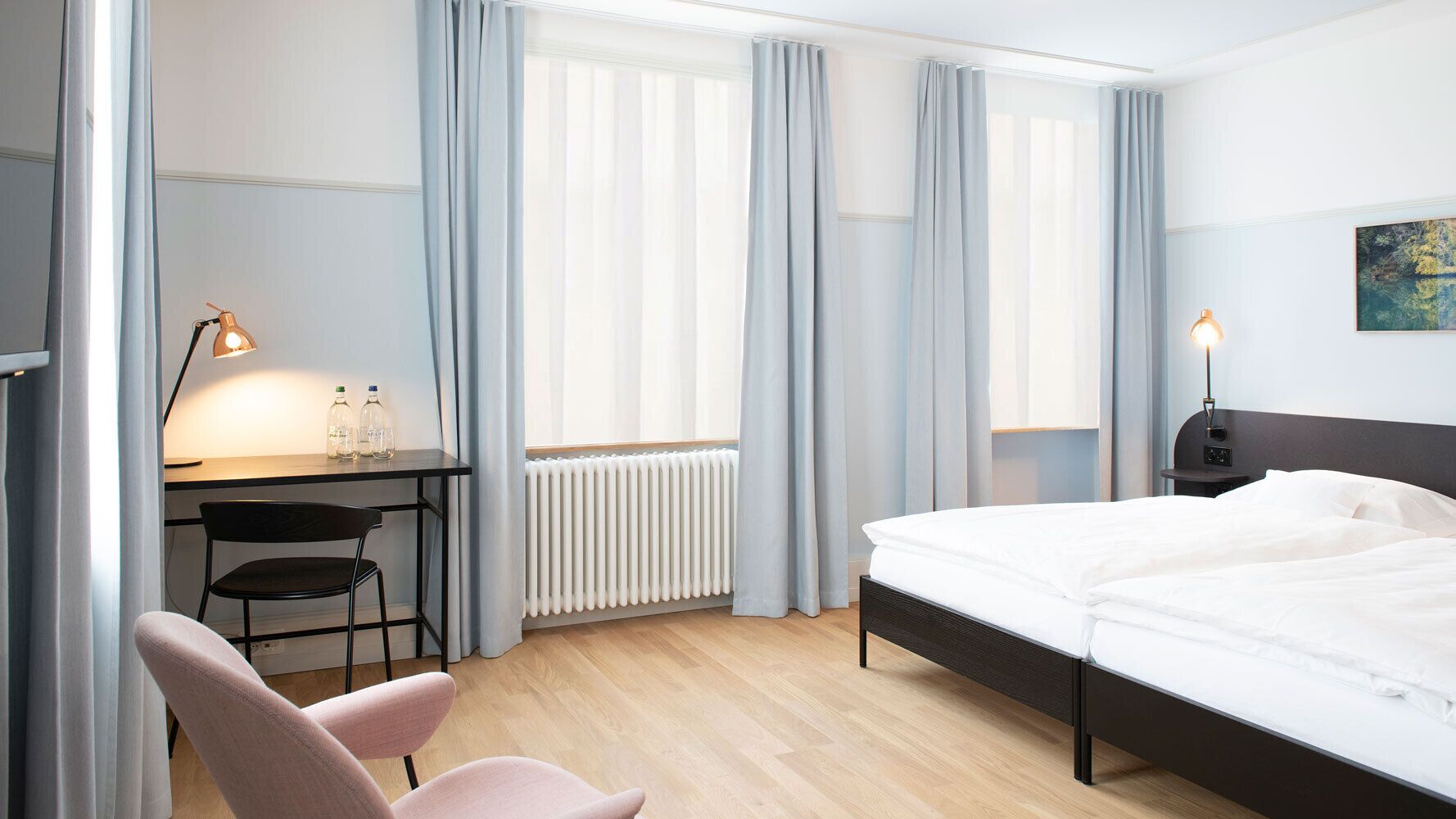 Une chambre d’hôtel avec un lit, un bureau, une chaise et un radiateur.