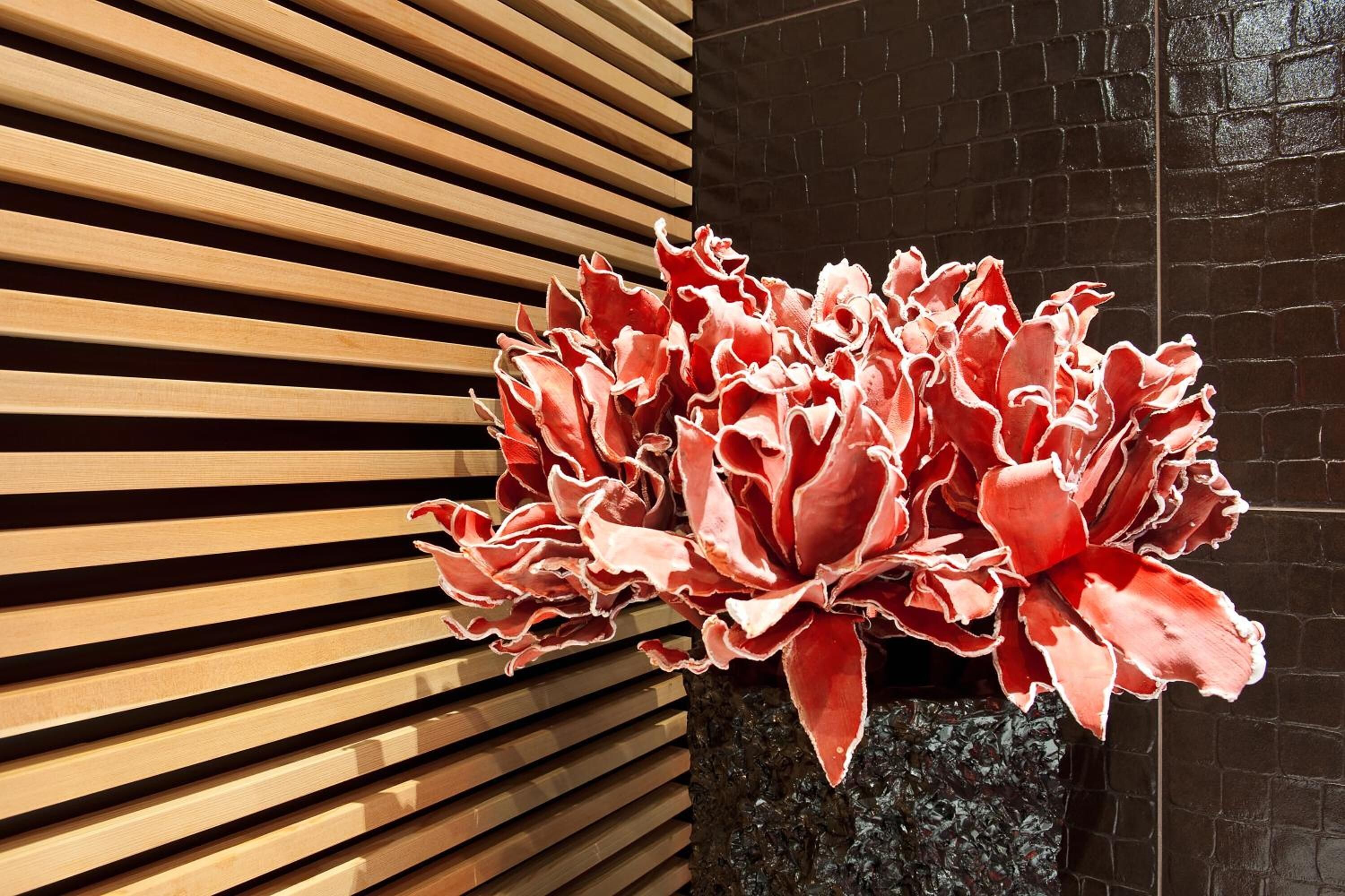 A potted plant with red foliage in front of a wooden slatted wall.