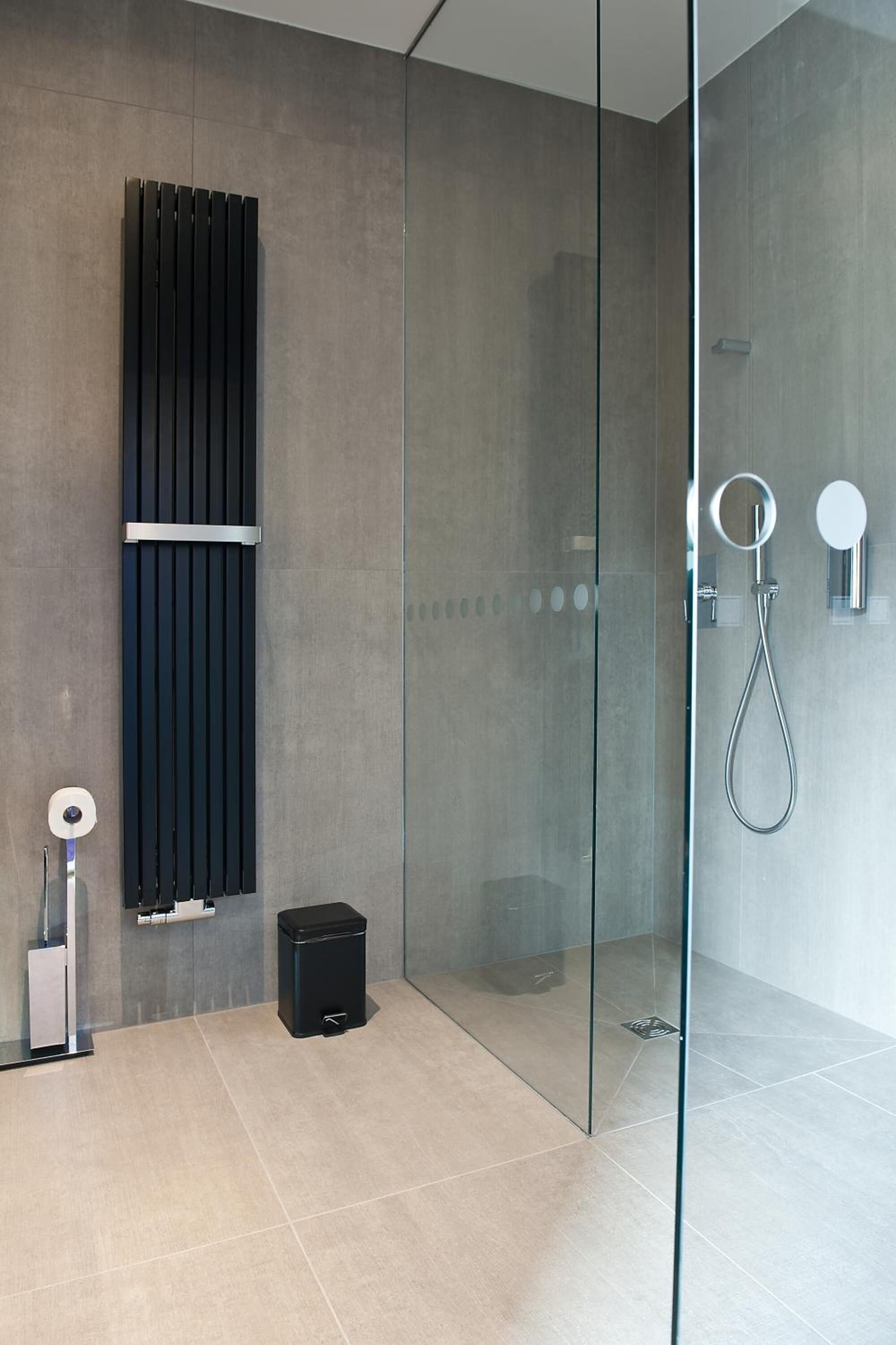 A modern bathroom with a glass shower enclosure, a black vertical panel, and a handheld showerhead.