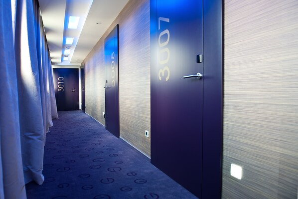Pasillo de hotel con puertas numeradas, alfombra estampada y diseño moderno.
