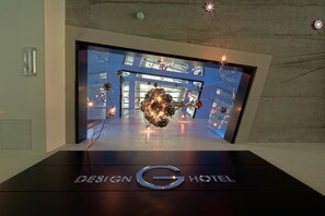 A modern hotel entrance with a digital display of a cityscape and a decorative sculpture. - G Design Hotel (Ljubljana)