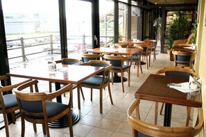 An indoor dining area with wooden tables and chairs, large windows, and a view of the outside. - Velga Hotel (Vilnius)