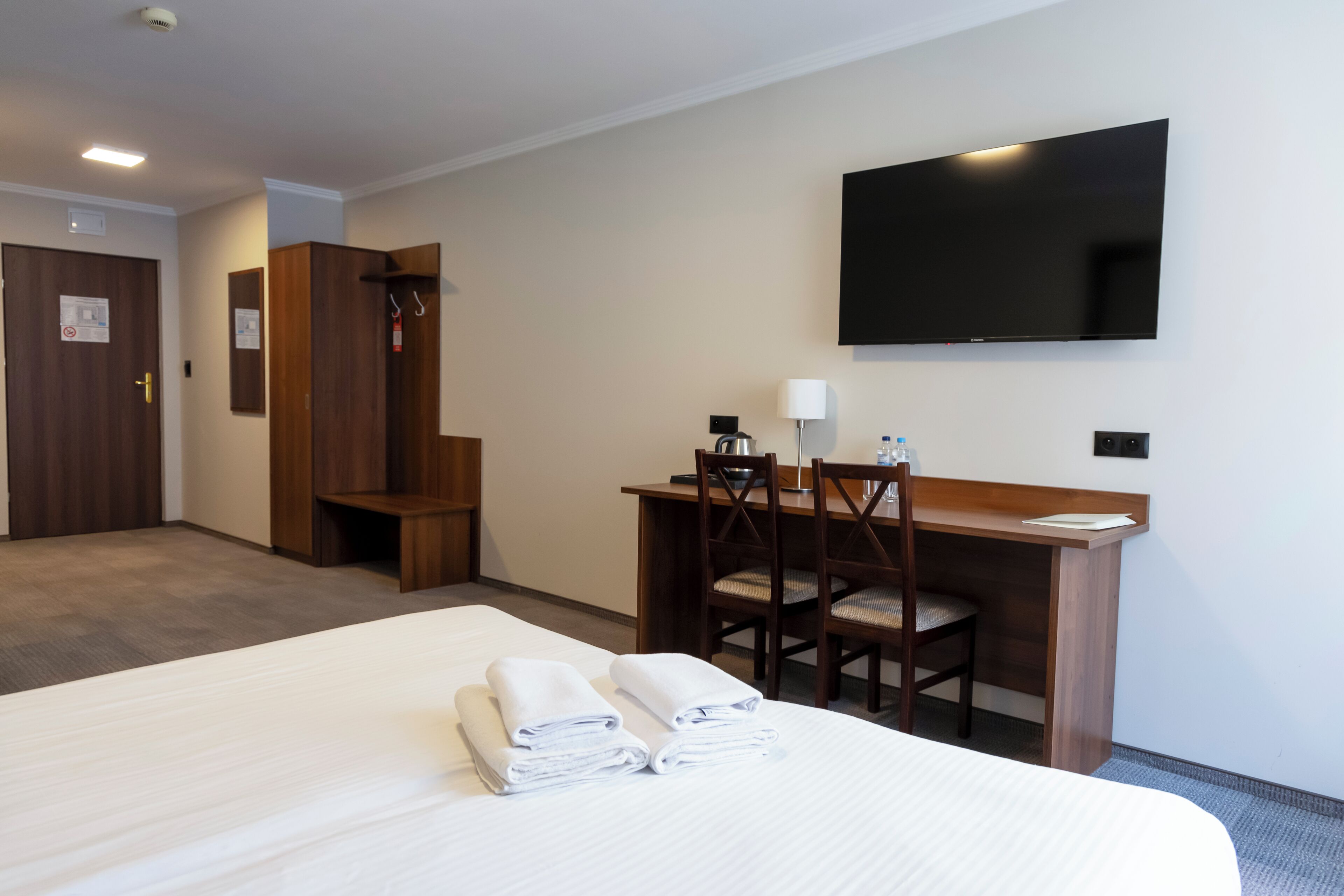 A hotel room with a bed, a desk with chairs, a flat-screen TV, and a coat rack.