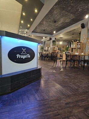 Interior de restaurant amb un disseny modern, amb un taulell central amb un logotip, terres de fusta i cadires negres.
