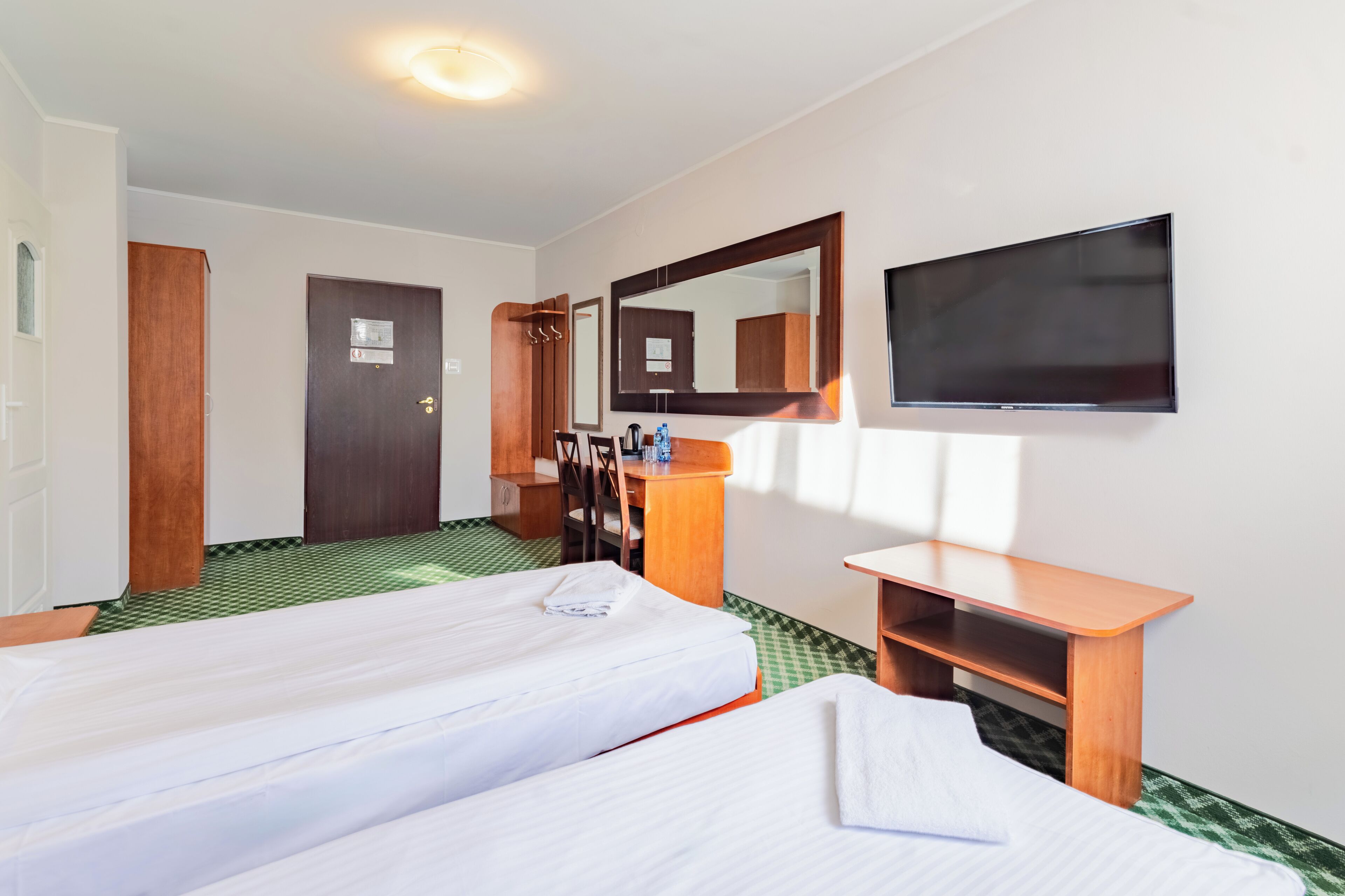 A hotel room with two beds, a desk, a chair, a mirror, and a TV.