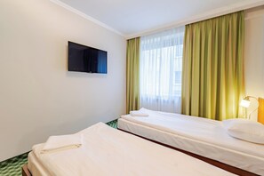 Habitación de hotel con dos camas, televisión de pantalla plana, ventana con cortinas traslúcidas y una lámpara de noche.