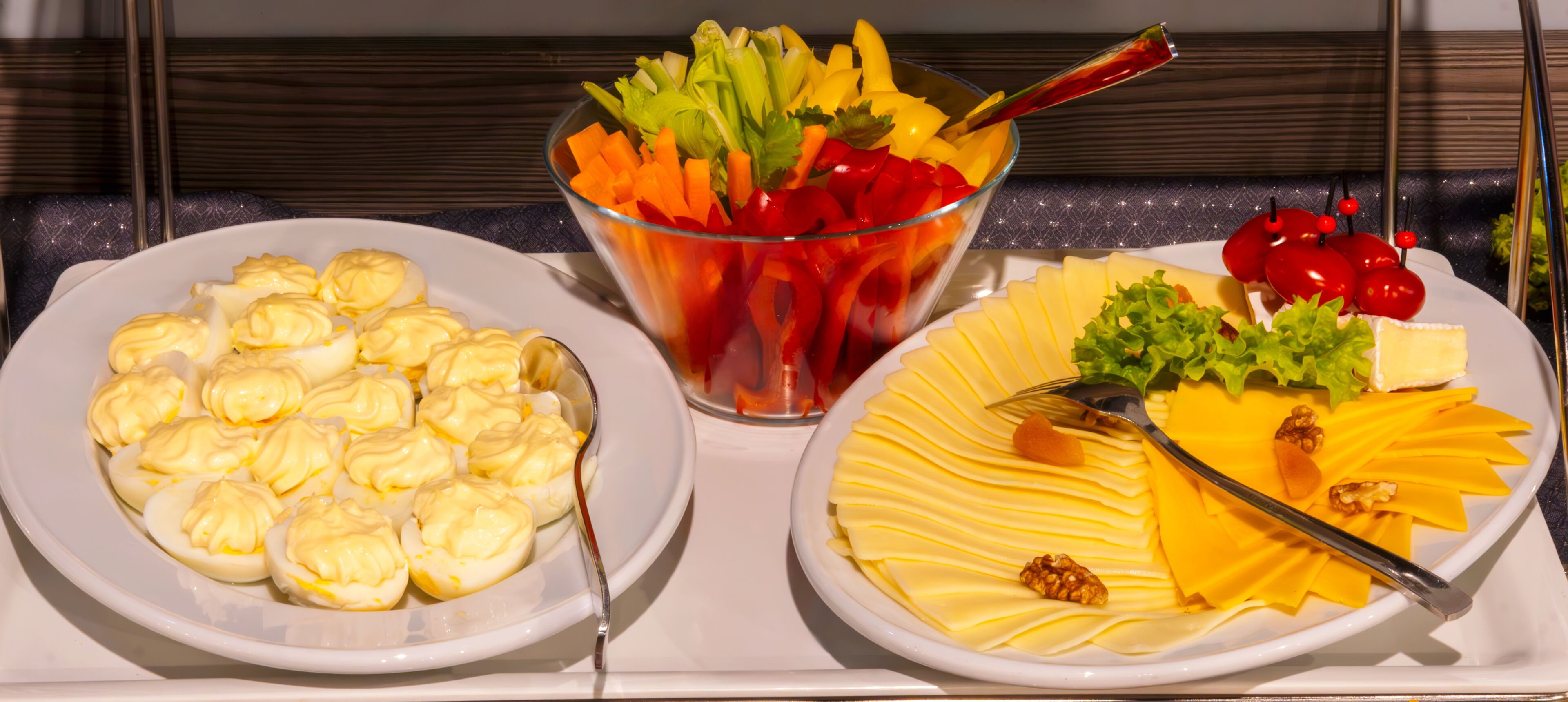 Three plates of food: one with boiled eggs, one with a salad, and one with cheese and nuts.