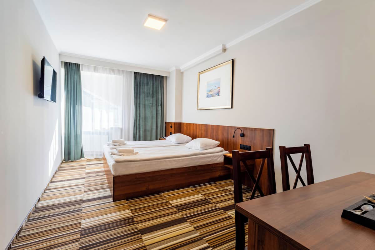Hotellihuone, jossa on sänky, puinen pääty, ruokapöytä ja seinälle asennettu televisio.