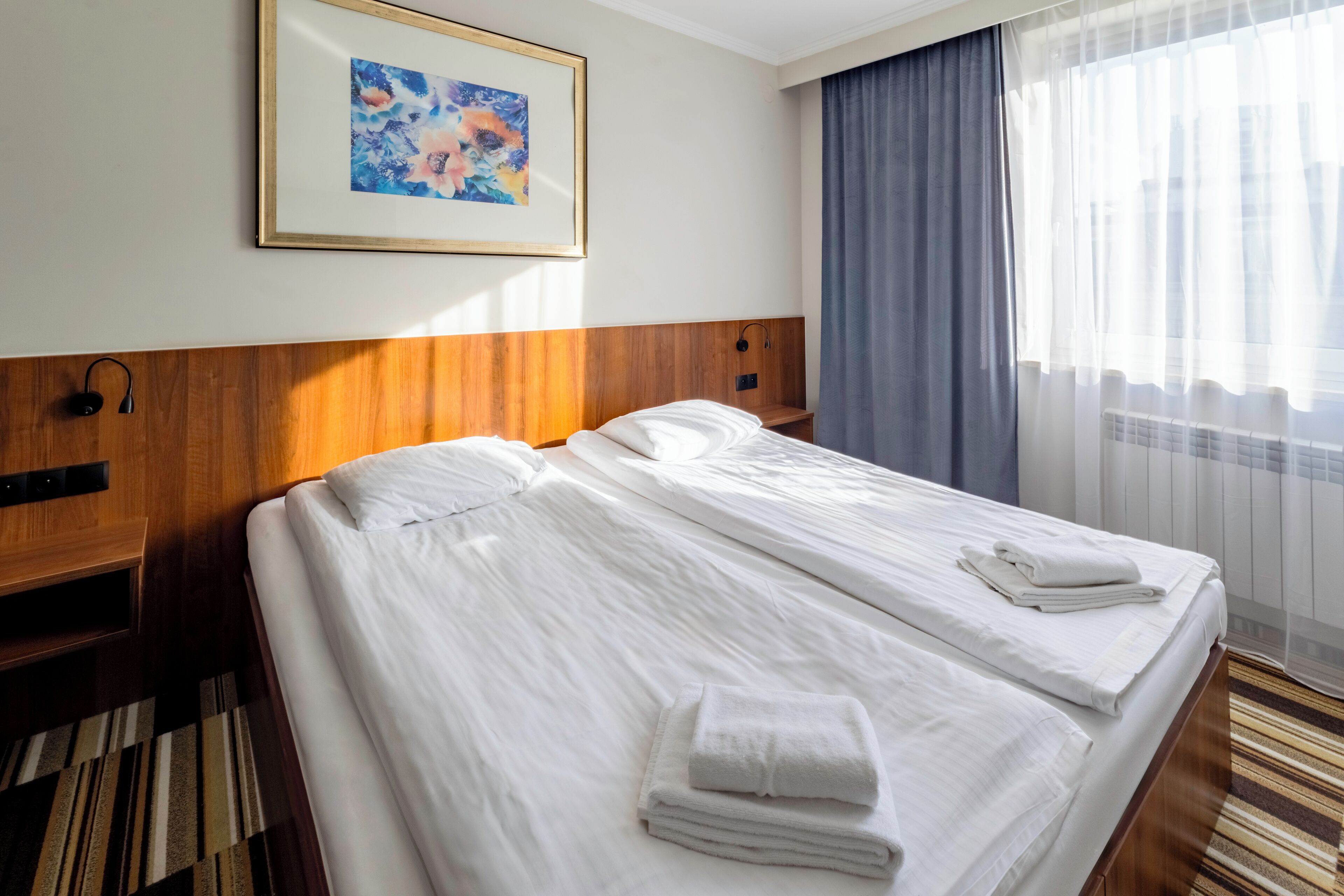 Una habitación de hotel con dos camas, un cuadro en la pared y una ventana con cortinas.