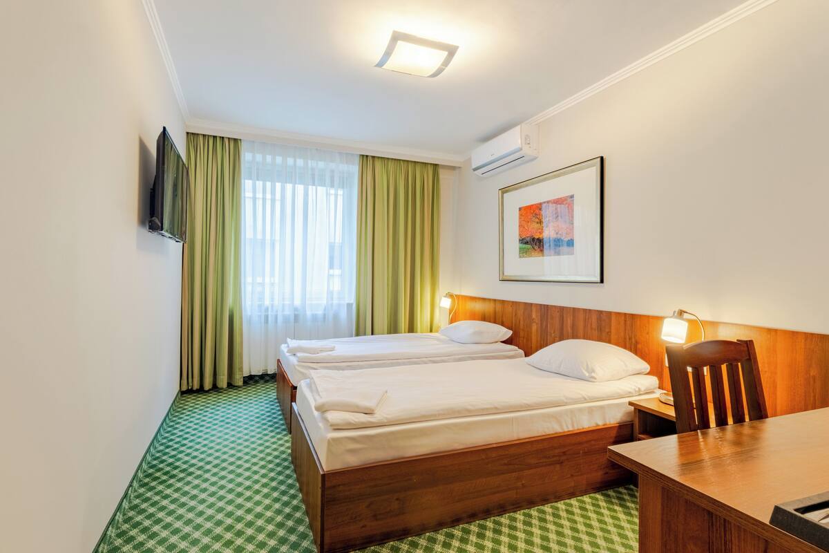 Hotellihuone, jossa on kaksi sänkyä, työpöytä, tuoli, televisio ja taulu seinällä.