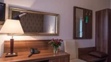A hotel room with a wooden desk, a chair, a lamp, a mirror, and a small plant.