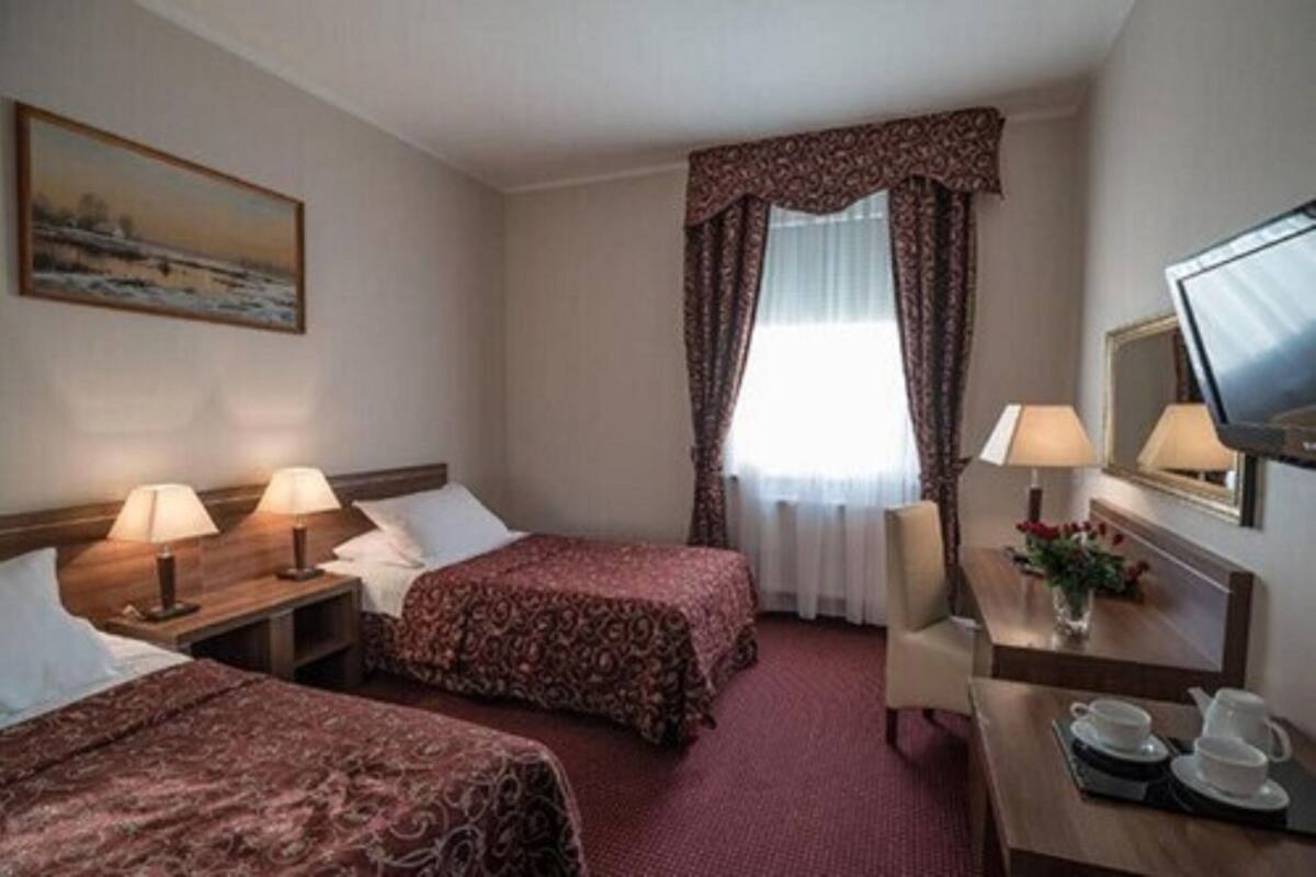 Une chambre d’hôtel avec deux lits, un bureau avec une chaise, une télévision et un tableau au mur.