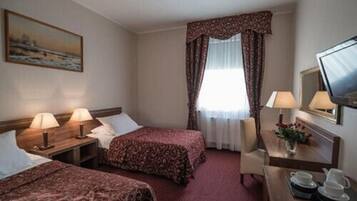 A hotel room with two beds, a desk with a chair, a TV, and a painting on the wall.