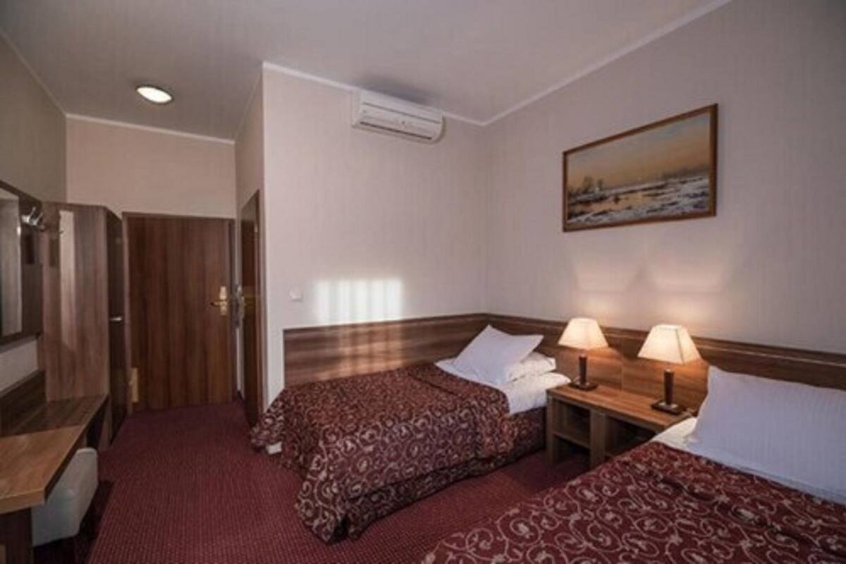 Une chambre d’hôtel avec deux lits, une tête de lit en bois, un tableau au mur et une petite table avec des lampes.