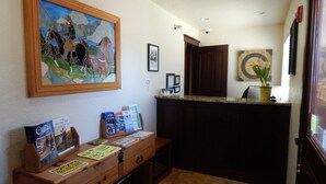 A reception area with a wooden desk, framed travel guides, a clock, and a painting on the wall. - Winterton Suites (Williston)