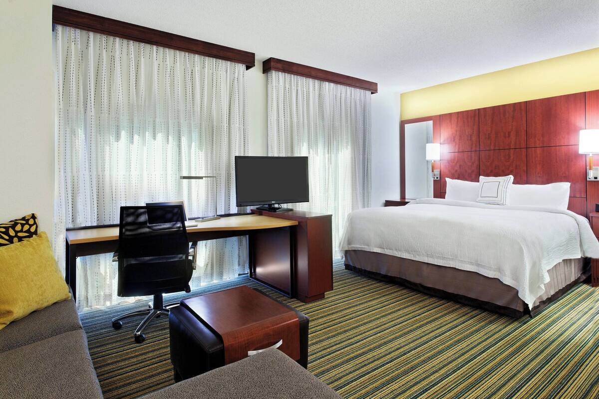 A hotel room with a bed, a desk with a computer, a TV, and a sofa.
