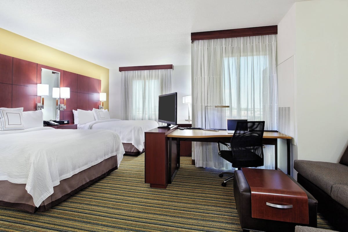 A hotel room with two beds, a desk, a chair, and a sofa.