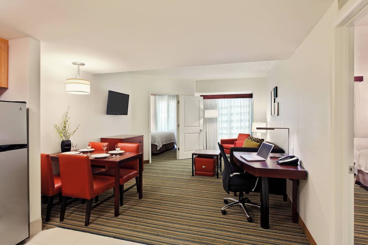 A hotel room with a dining area, a bed, a desk with a laptop, and a TV on the wall.