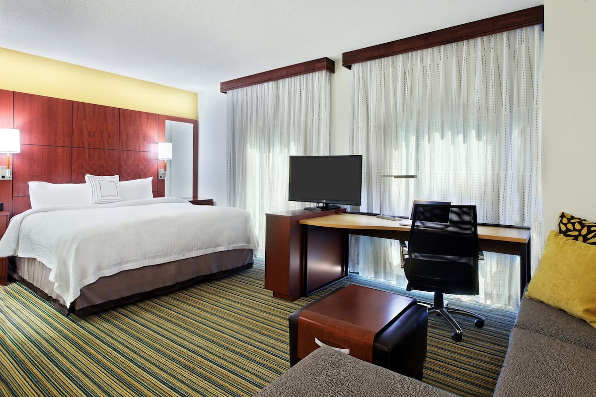 A hotel room with a bed, desk, chair, TV, and a sofa.