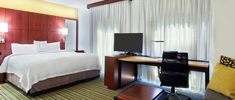 Une chambre d’hôtel équipée d’un lit, d’un bureau, d’une chaise, d’une télévision et d’un canapé.