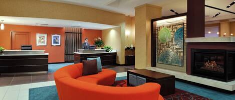 A hotel lobby with a reception desk, a fireplace, a large painting, and a modern orange sofa.