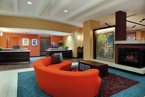 A hotel lobby with a reception desk, a fireplace, a large painting, and a modern orange sofa.
