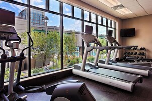 Un gimnasio con cintas de correr, elíptica y mancuernas, con amplias ventanas que ofrecen vistas a edificios y árboles.