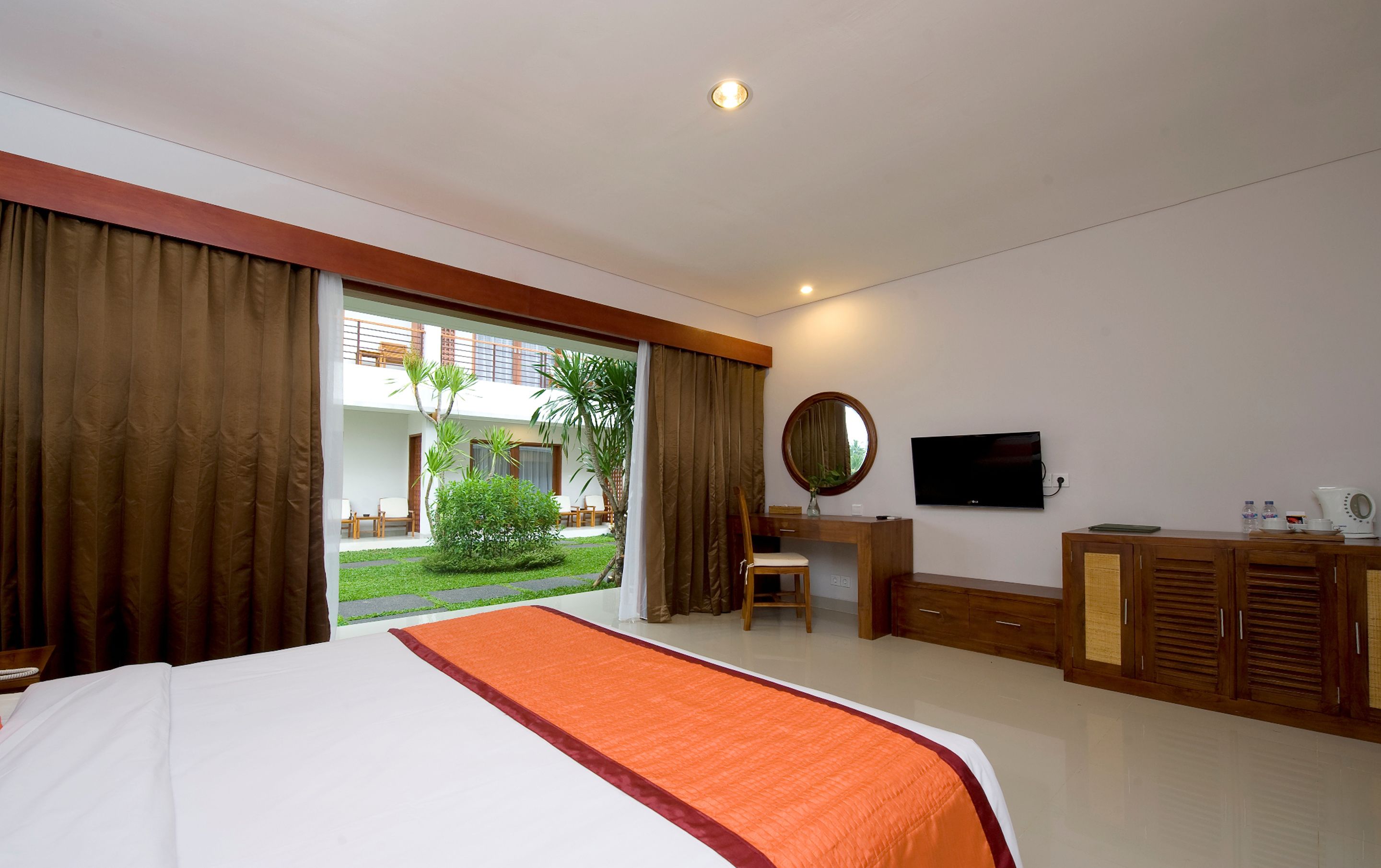 A hotel room with a bed, a desk, a TV, and a view of the outdoor area.