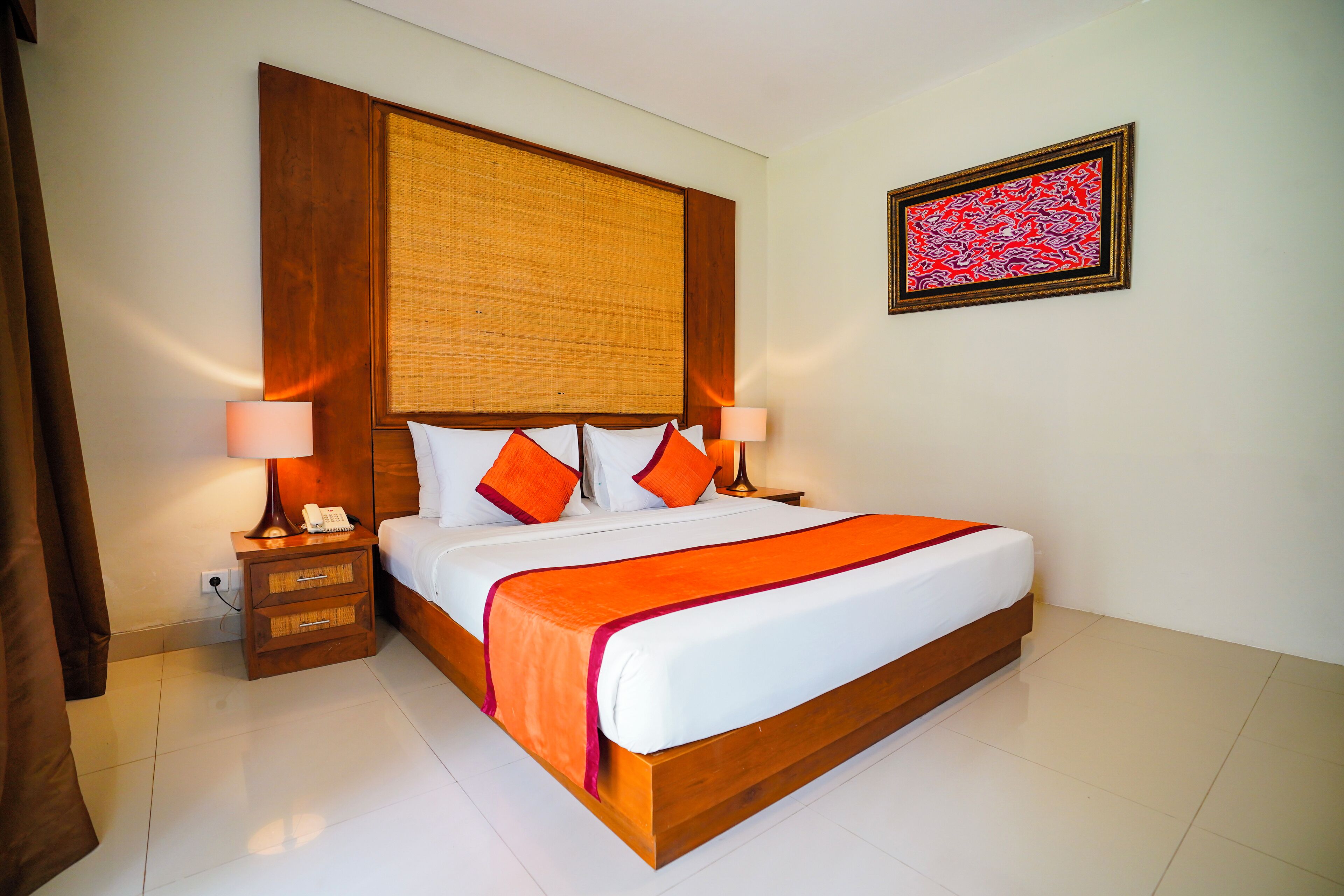 A hotel room with a large bed, wooden headboard, two bedside tables with lamps, and a wall-mounted artwork.