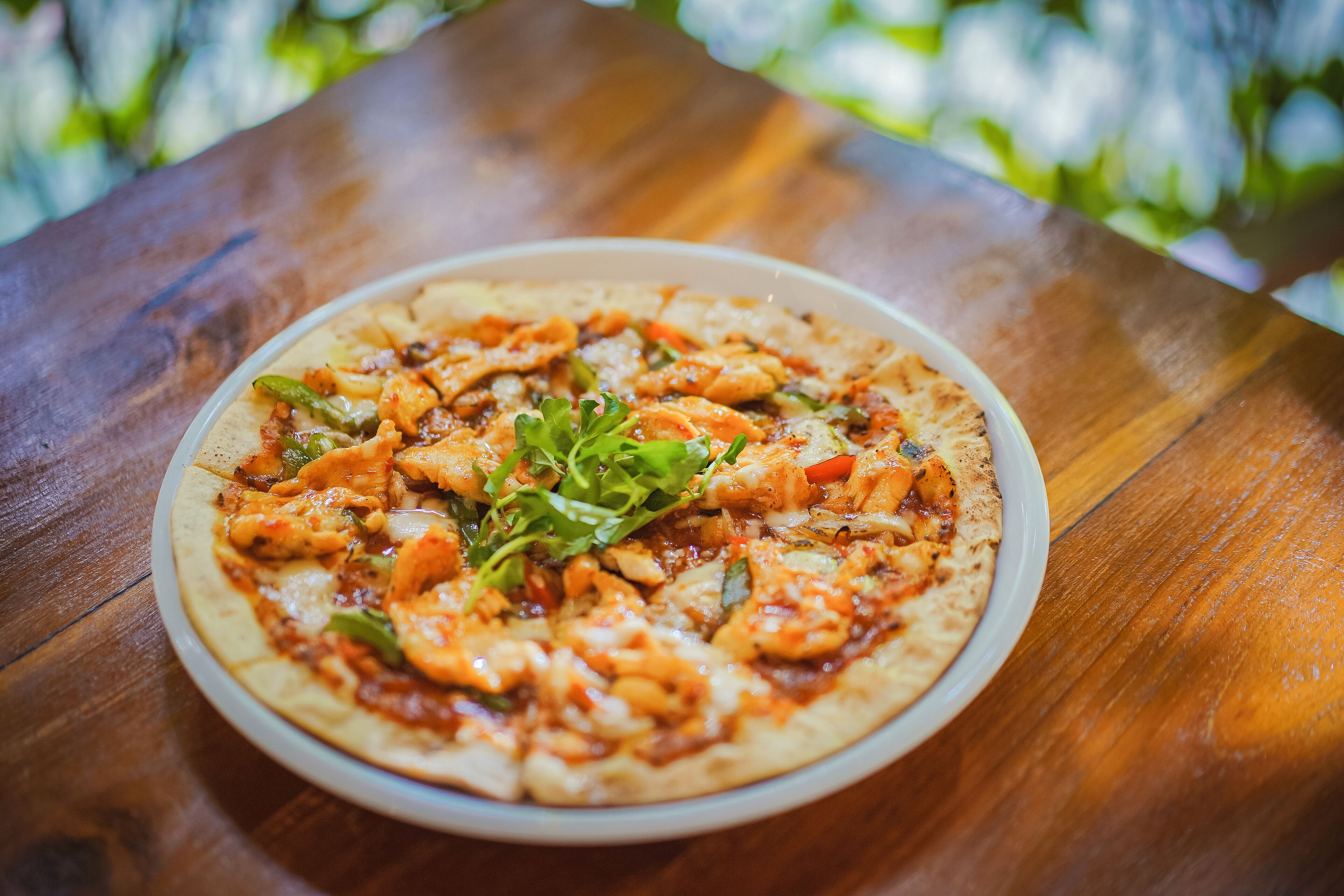 A pizza on a white plate on a wooden table.