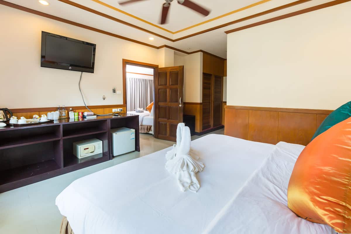 A hotel room with a bed, a TV mounted on the wall, a wooden wardrobe, and a desk with toiletries.