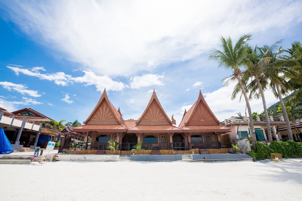 A traditional multi-tiered building with a symmetrical roof design, situated on a sandy beach with palm trees in the background.