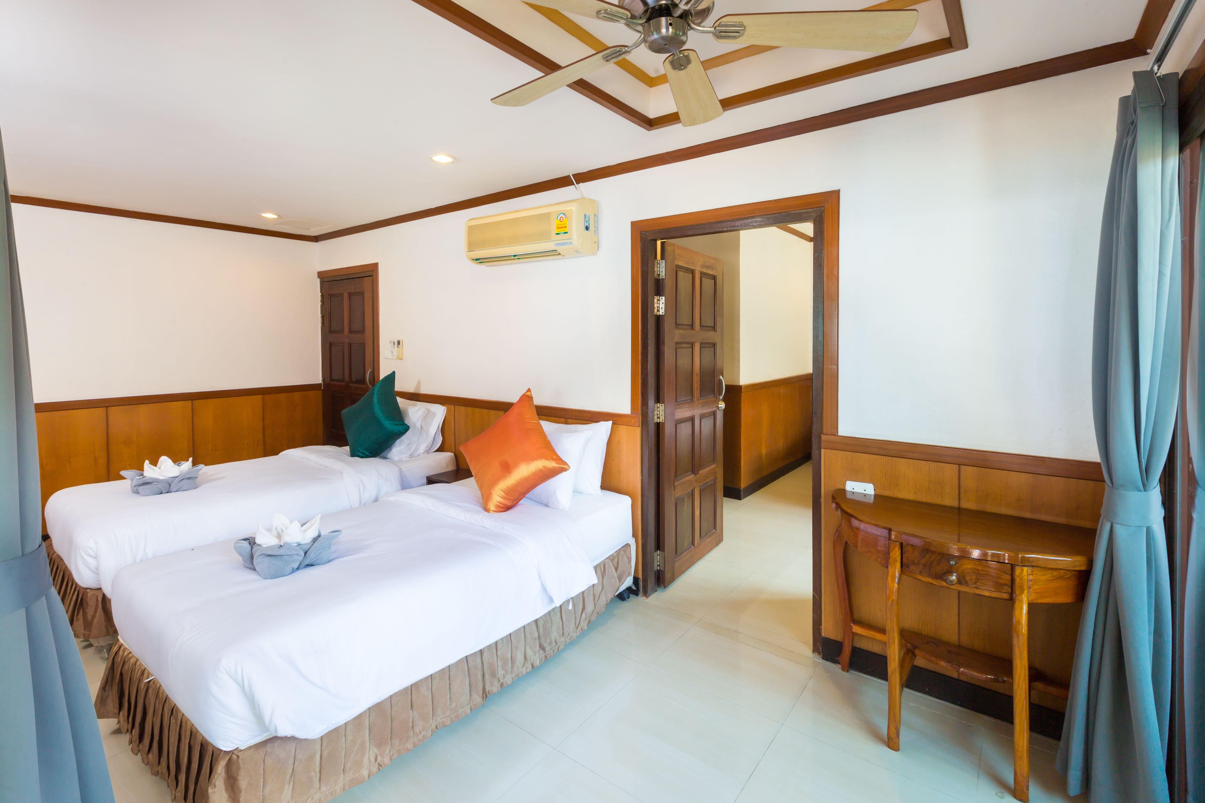 Ein Hotelzimmer mit zwei Betten, einem Holztisch, einem Deckenventilator und einer Klimaanlage.