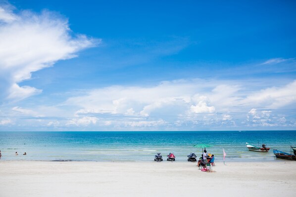 Una playa con agua azul cristalina, algunas personas y embarcaciones.