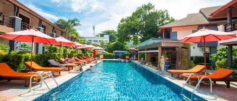 A swimming pool with lounge chairs and umbrellas, surrounded by buildings.