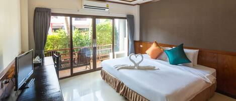 Habitación de hotel con cama, escritorio con computadora, ventilador de techo y puerta corrediza de vidrio al exterior.