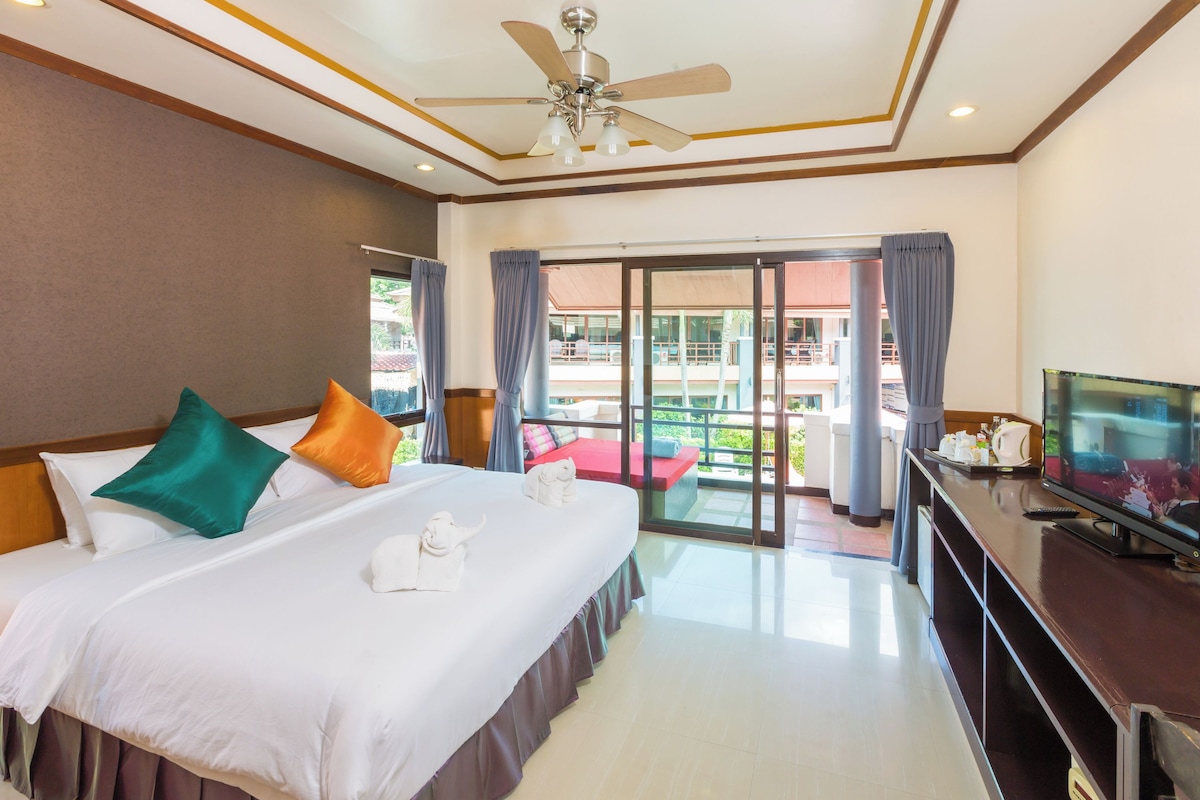 A hotel room with a bed, a TV, a ceiling fan, and a balcony with a view.