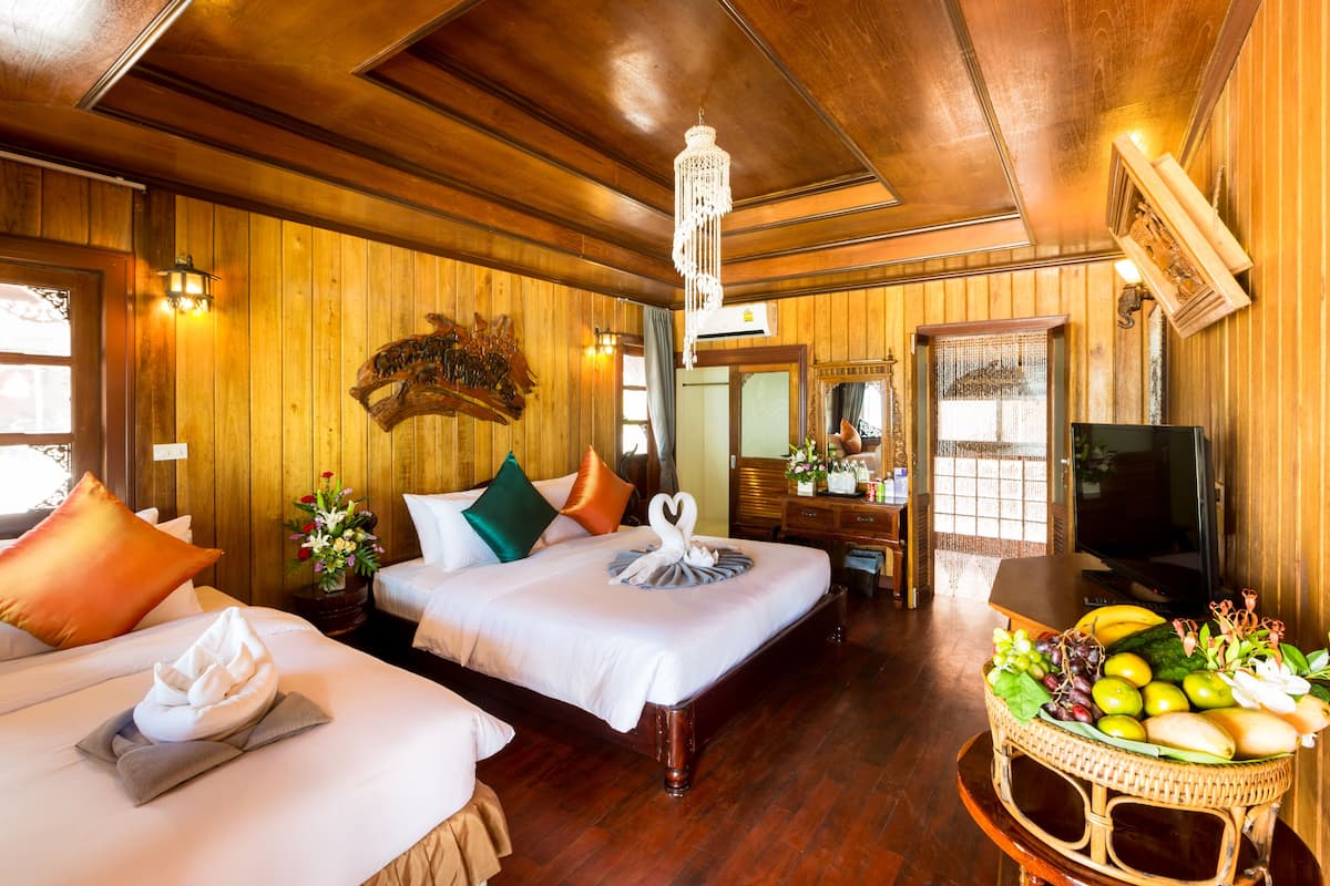 A hotel room with two beds, wooden walls, a chandelier, a television, and a fruit basket.