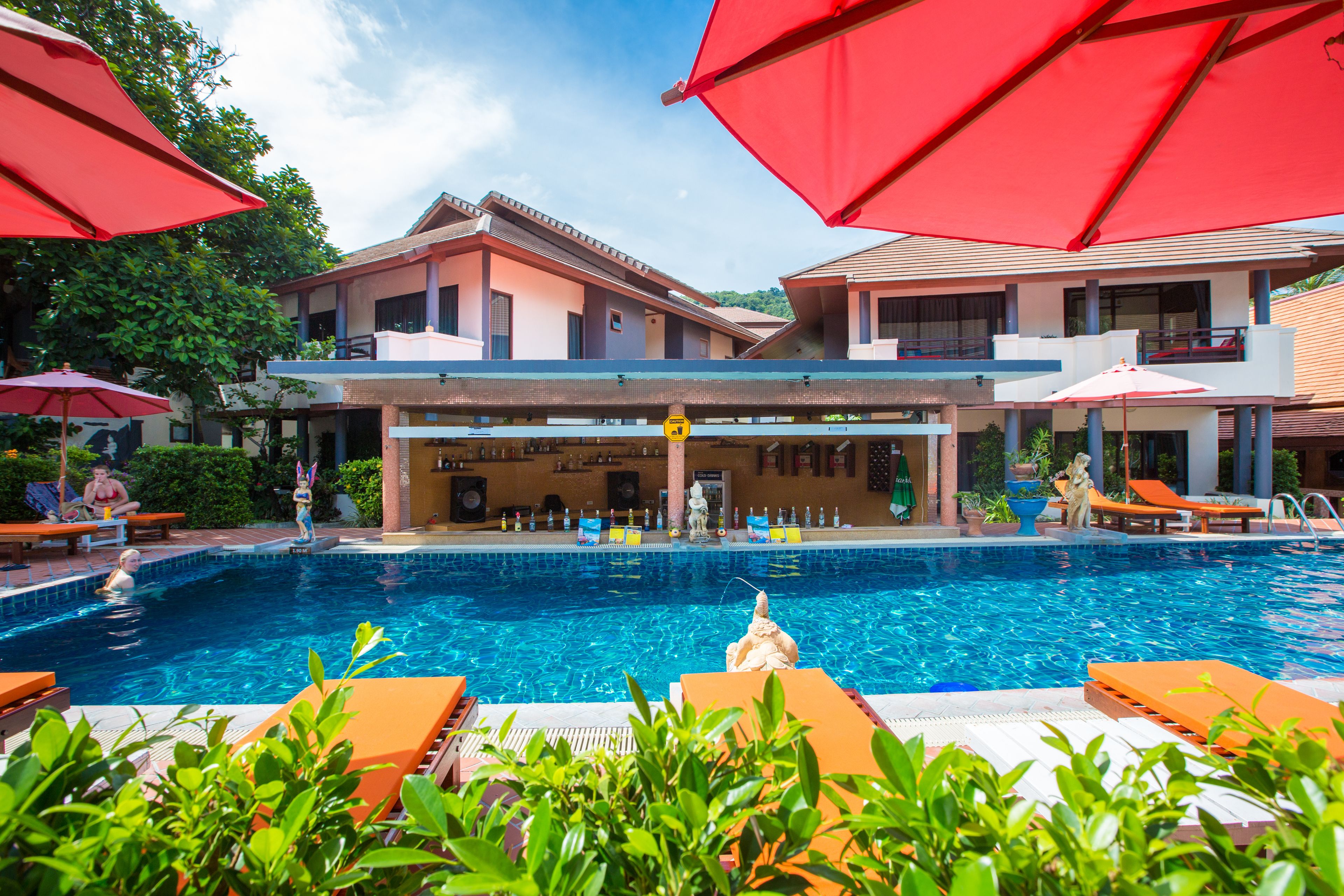A swimming pool area with lounge chairs and umbrellas, surrounded by buildings with balconies.