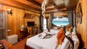 A wooden-themed hotel room with a bed, a television, a minibar, and a view of the beach. - Sunrise Resort (Ko Pha-ngan)