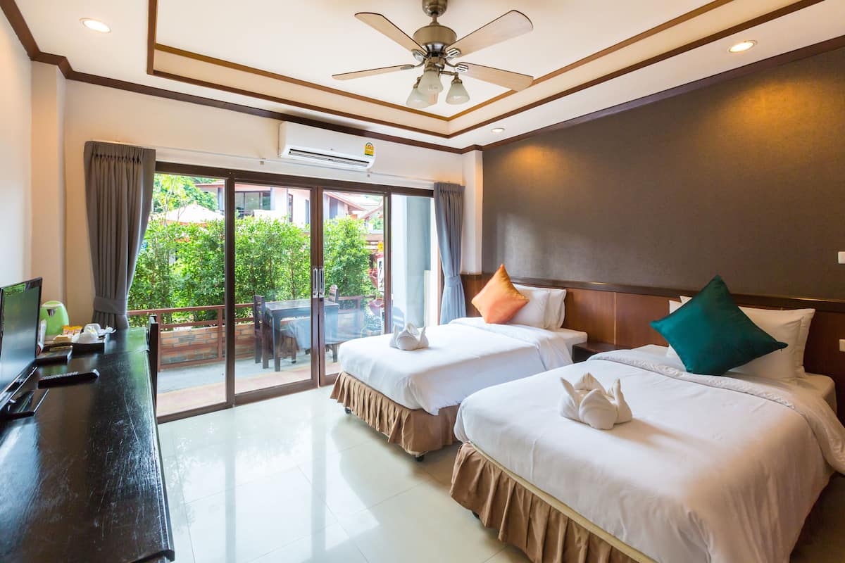 A hotel room with two beds, a TV, and a balcony with a view of greenery.
