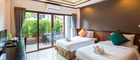 Habitación de hotel con dos camas, televisión y balcón con vista a zonas verdes.