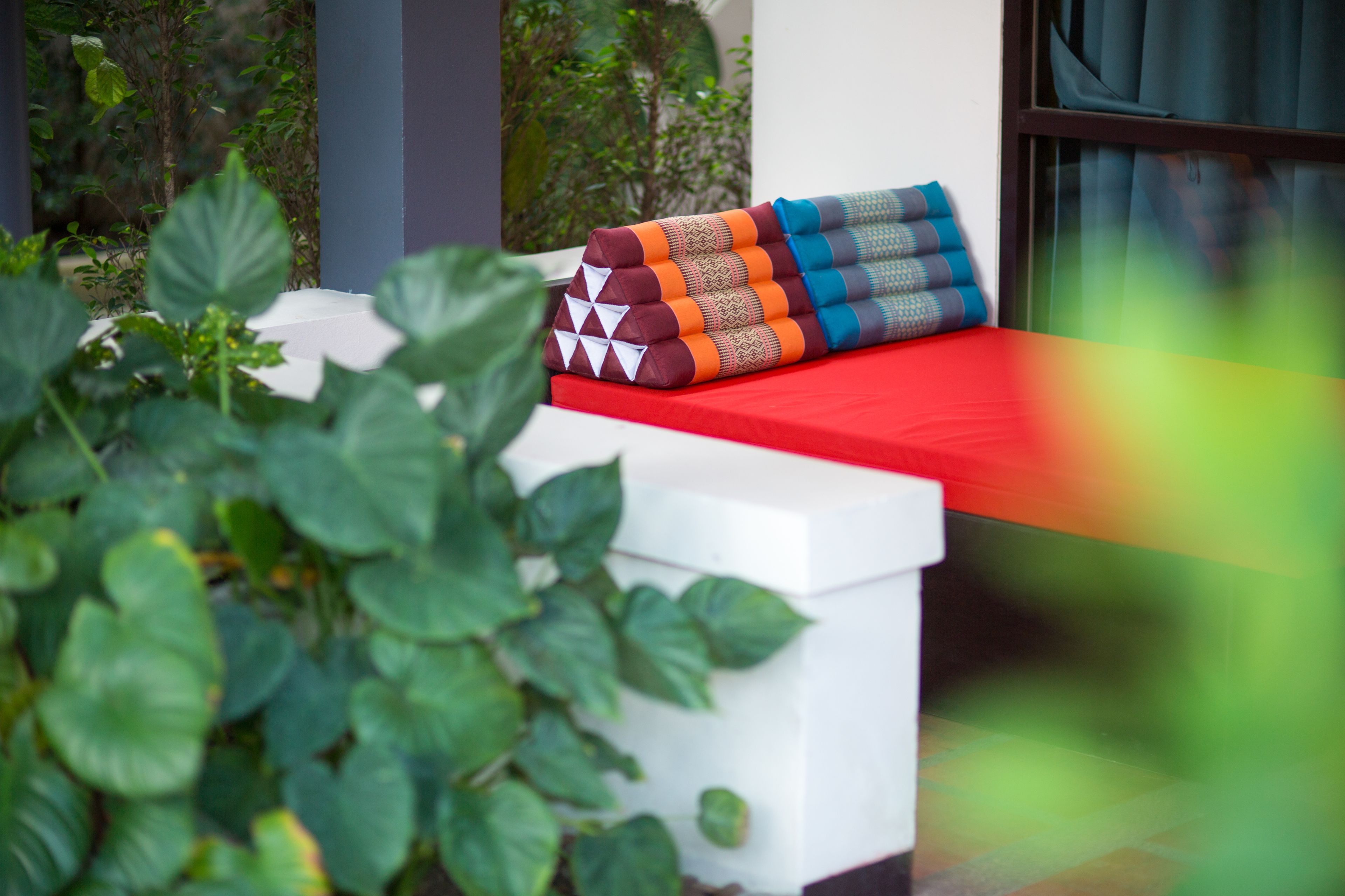 A white outdoor seating area with a red cushion and patterned cushions.