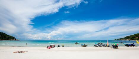 A beach with white sand, clear blue water, and boats.