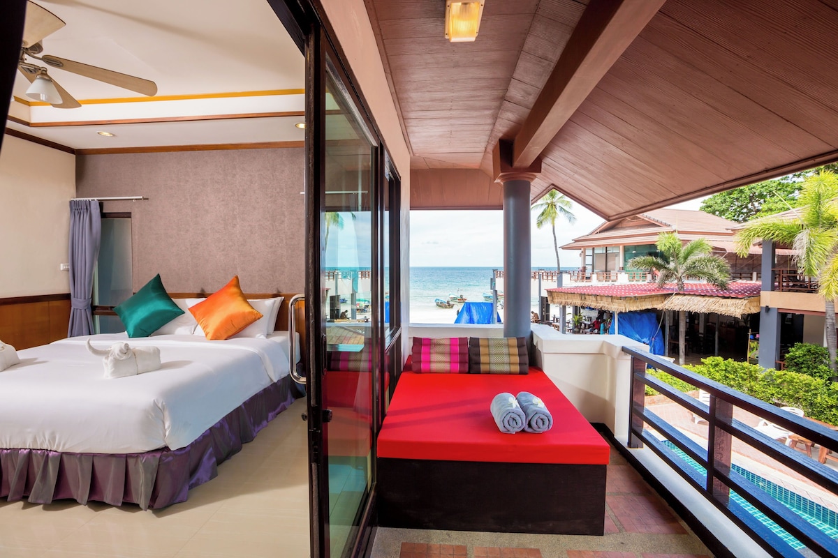 A hotel room with a balcony, a bed, a red bench, and a view of the beach and ocean.