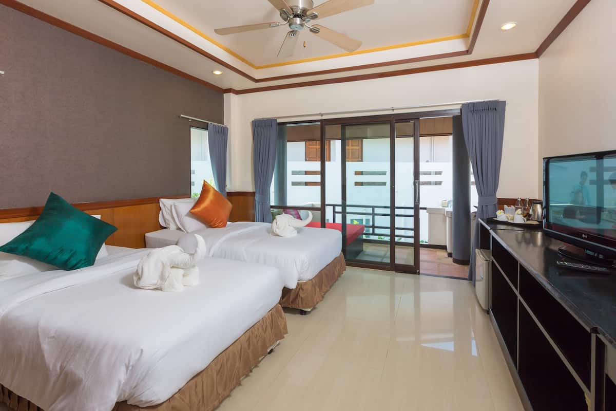 A hotel room with two beds, a ceiling fan, a television, and a balcony with curtains.